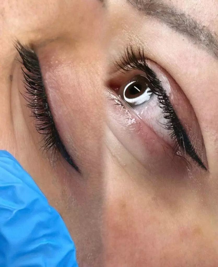 A woman's eye is being treated with eyelash extensions at home.