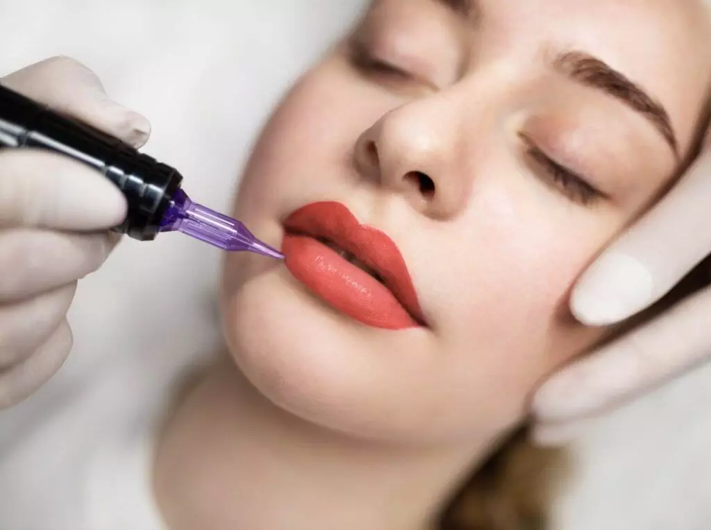 A person undergoing a lip blushing procedure with purple tattoo equipment and gloved hands visible, highlighting the benefits of this cosmetic treatment in San Diego.