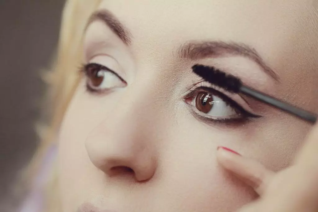 Close-up of a person applying mascara with a brush to their eyelashes, carefully avoiding any smudging.