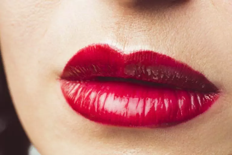 Close-up image of lips with bright red lipstick, showing light reflection and smooth application that reveals a perfect pout.