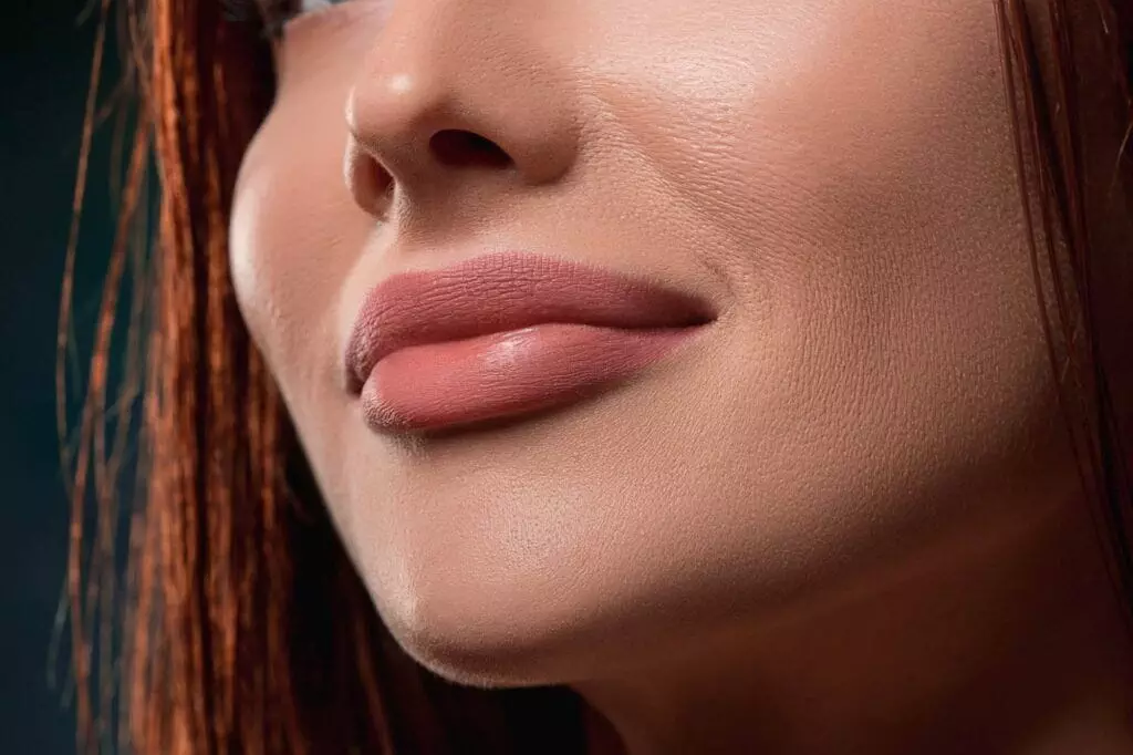 Close-up of a woman's lower face showing her nose, lips, and part of her cheek with smooth skin and a slight smile, enhanced by a perfect pout.